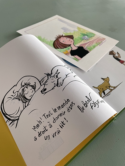 The comic book 'Margot et Oscar, Jardin Secret', is opened on its first page. De Brab had put a drawing of Margot sleeping with the dog Oscar on her lap. A text reads: "Everyone deserves to sleep in his/her own bed."